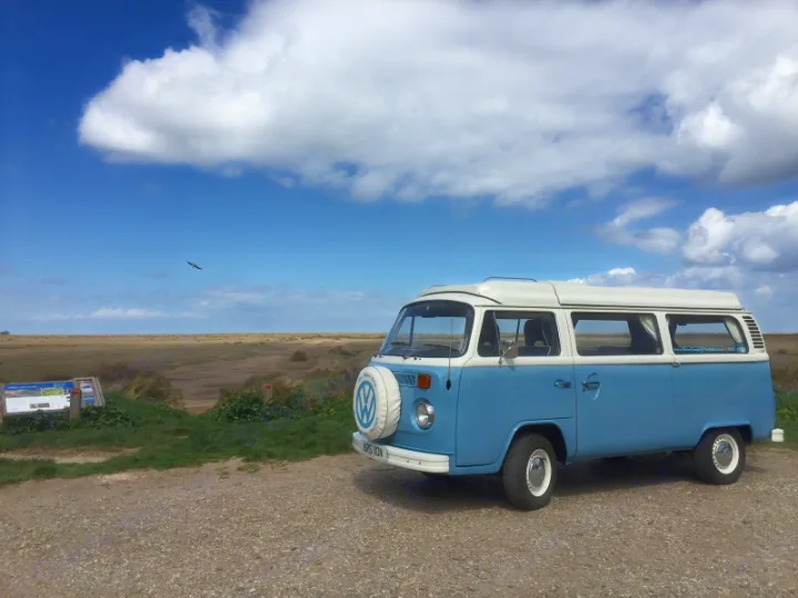Classic light blue and white VW camper for your RV rental adventure. Parked overlooking marshlands under a cloudy blue sky.. Volkswagen 2.0L T2 Late Bay 1975