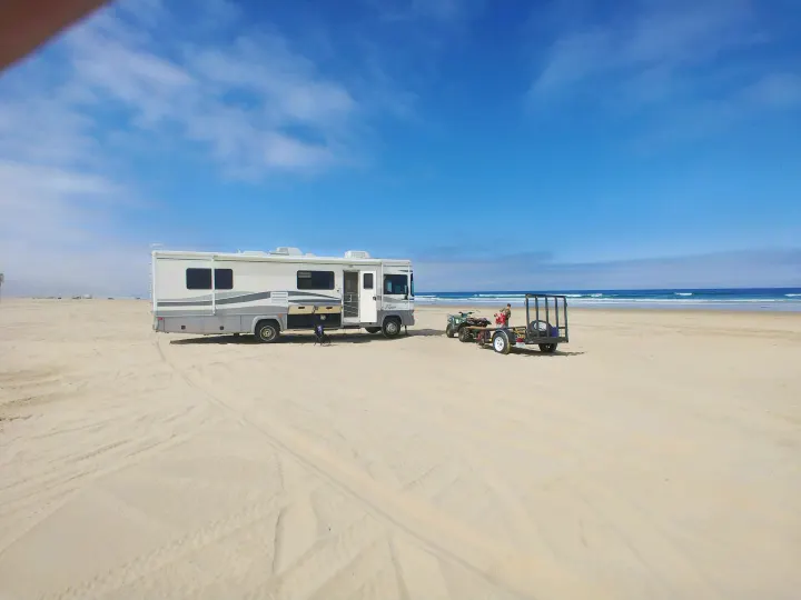 RV rental parked on a vast sandy beach with an ATV trailer, offering direct ocean access for beach camping.. Fleetwood Flair 2000