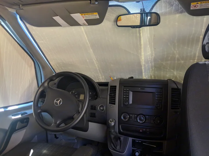 Mercedes-Benz van interior, possibly an RV rental, with dashboard, steering wheel, and sunshade providing privacy.. Mercedes-Benz Sprinter 2016