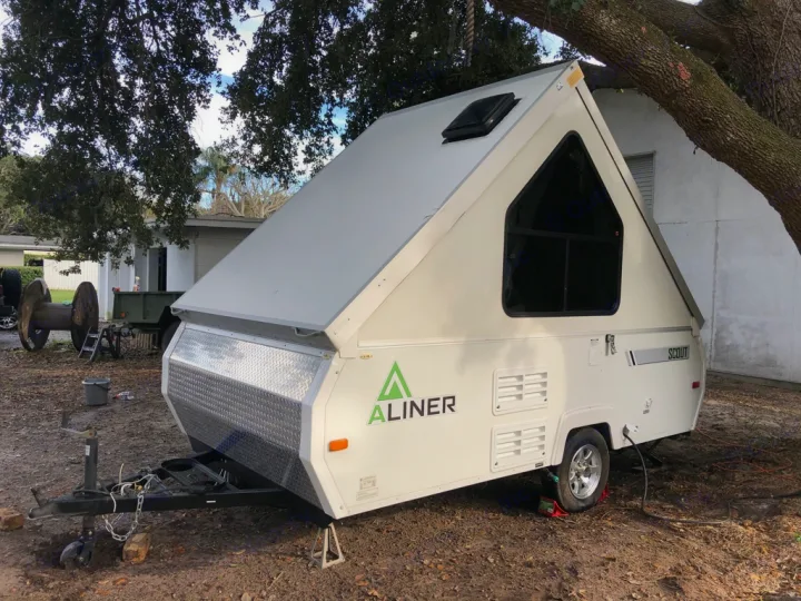 A white A-Liner Scout pop-up RV, great for an rv rental, is seen deployed in a yard with trees.. A-Liner Scout 2013