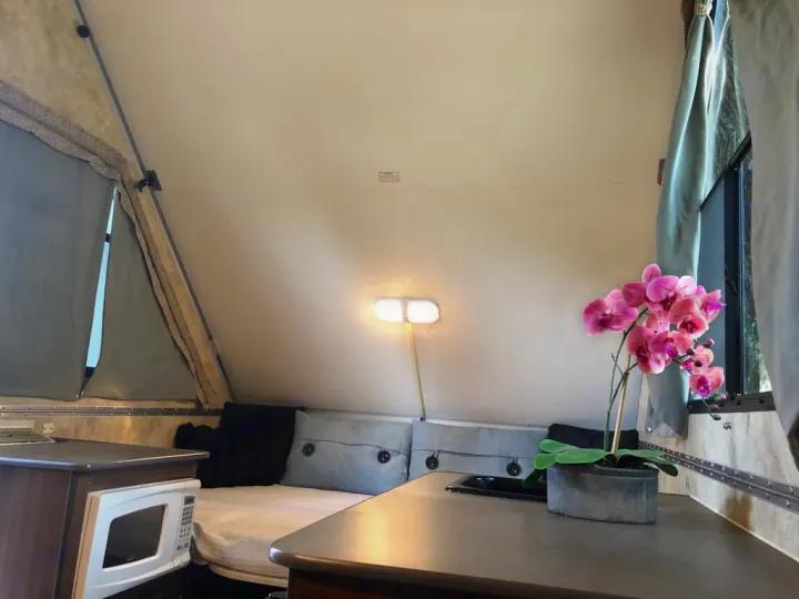 Explore this cozy A-frame camper RV rental interior! Features a compact kitchenette, comfortable bed, and lovely decor.. A-Liner Scout 2013