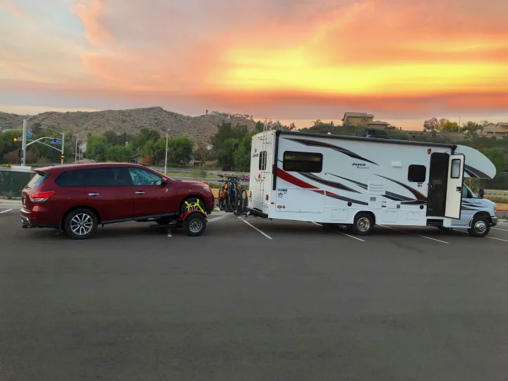 Stunning sunset frames an RV rental: Jayco Redhawk towing a red Pathfinder on a dolly with bikes. Ready for adventure!. Jayco Redhawk 2019