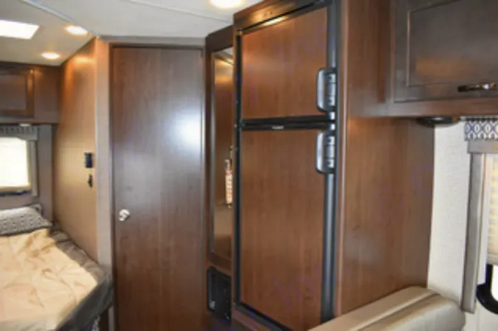 RV rental interior: compact space with a two-door refrigerator, wood cabinetry, and a cozy sleeping area.. Thor Motor Coach Freedom elite 23 H 2019