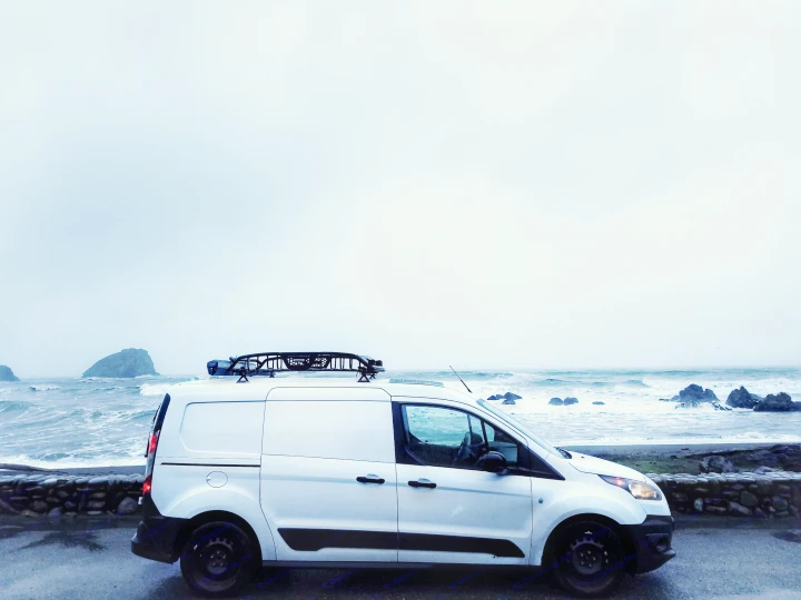 A white van, perfect for RV rental, parked by a stormy ocean with crashing waves, rocks, and an overcast sky.. Ford Transit Custom 2017