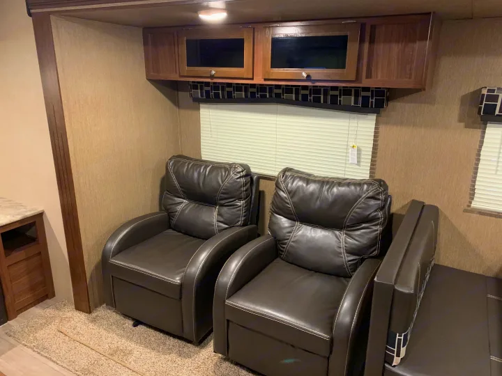 RV rental living area featuring two dark leather recliners, overhead cabinets, and a window with blinds.. Coleman Lantern 2018