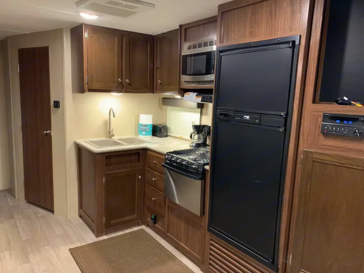 This clean RV rental features a full kitchen with dark wood cabinets, sink, microwave, stove, and fridge, ready for use.. Coleman Lantern 2018