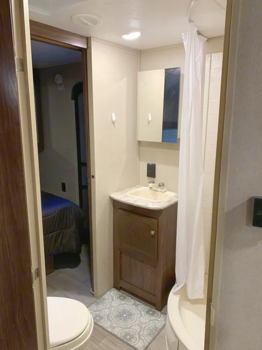 An rv rental's bright bathroom, featuring a white shower curtain, a vanity with sink and mirror, and a toilet. Compact layout.. Coleman Lantern 2018