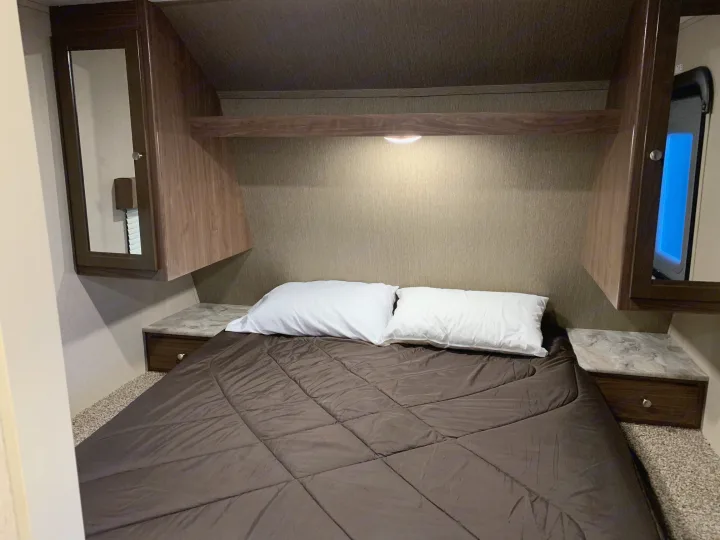 Cozy RV rental bedroom featuring a bed with white pillows, mirrored cabinets, and a window for natural light.. Coleman Lantern 2018