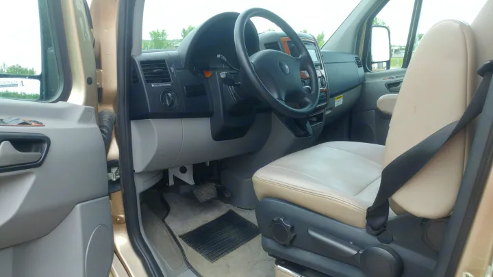 Driver's side interior of an RV rental, featuring the tan seat, steering wheel, and dashboard. View of the cockpit area.. Roadtrek Roadtrek Class B 2010