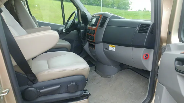 Cabin view of an RV rental, featuring the dashboard, steering wheel, and front beige leather passenger seat.. Roadtrek Roadtrek Class B 2010