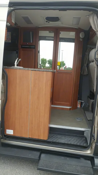 View of an rv rental interior: a compact kitchenette with wood cabinetry, sink, appliances, and front cabin.. Roadtrek Roadtrek Class B 2010