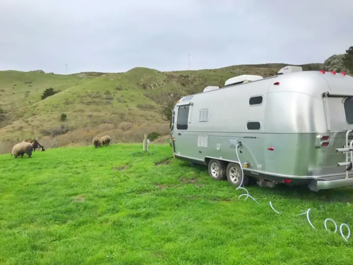 Experience an RV rental! Silver Airstream in a green field with grazing sheep & rolling hills. Perfect nature escape.. Airstream Safari 2008