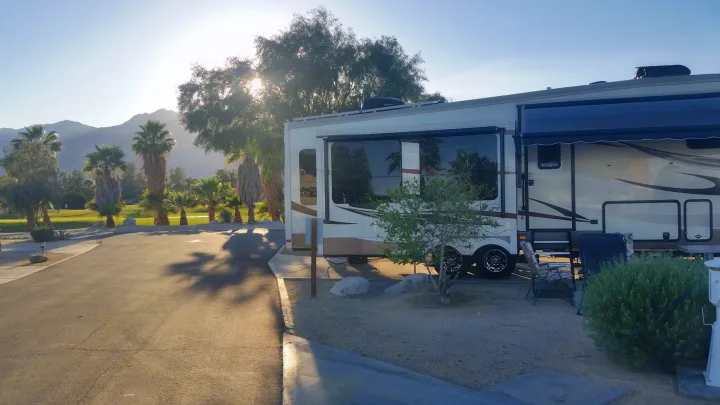 Relaxing RV rental setup at a desert campsite, featuring palm trees, mountains, and morning sun. Ideal for travel.. Forest River Cardinal 2017