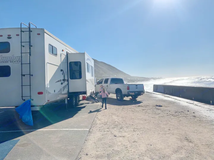 Scenic coastal RV rental adventure: A fifth wheel and truck parked by the ocean with kids exploring. Perfect family getaway.. Palomino Columbus 2018