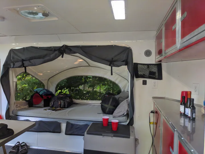This RV rental's interior features a cozy pop-up bed with forest views, red cabinets, and a portable fridge for travel.. United XLMTV-610 2018