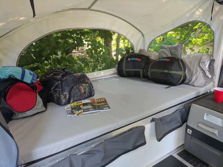 Inside a comfy RV rental: sleeping bags, camping gear, magazines on the bed, and a portable refrigerator.. United XLMTV-610 2018