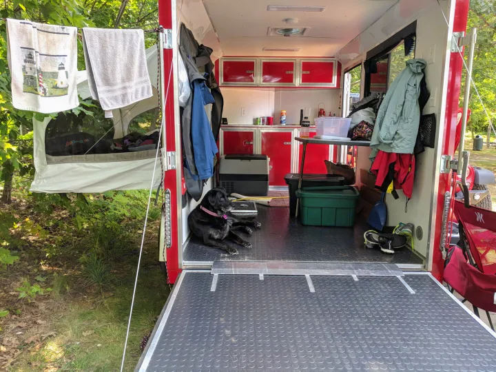 Converted RV rental interior at a lush campsite, featuring a dog, kitchenette, and outdoor drying towels.. United XLMTV-610 2018