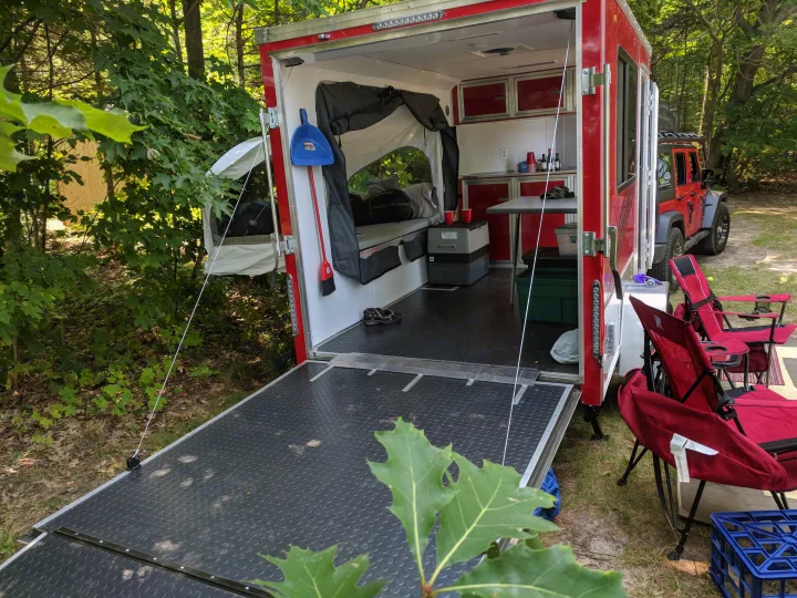 RV rental: Red camper with an open ramp and kitchen, set up at a wooded campsite next to a red Jeep. Perfect for outdoor escapes.. United XLMTV-610 2018
