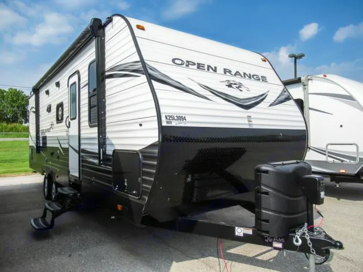 White and black Open Range RV rental travel trailer, featuring an awning, entry steps, and front propane tanks.. Openrange 26BHS 2020