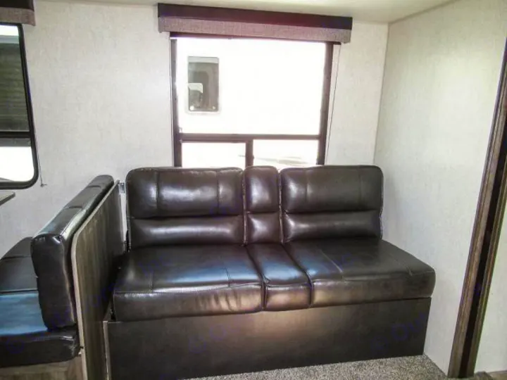Comfortable RV rental living area with dark sofa and dinette seating, illuminated by large windows.. Openrange 26BHS 2020