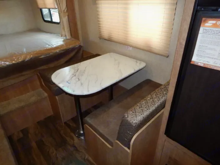 Inside an rv rental: Dinette featuring a marble-look table & patterned benches, a bed with plastic cover, and refrigerator.. Starcraft Launch 19BHS 2017