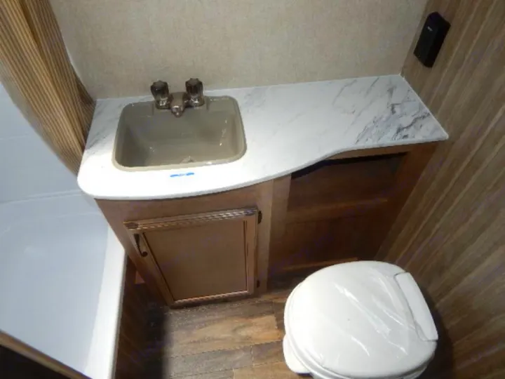 Compact RV rental bathroom features a white sink, counter, wooden vanity, shower, and toilet with plastic wrap.. Starcraft Launch 19BHS 2017