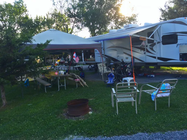 An RV rental is set up at a vibrant campsite, featuring an extended awning, outdoor chairs, tables, and a fire pit.. Keystone BulletPremier 2012
