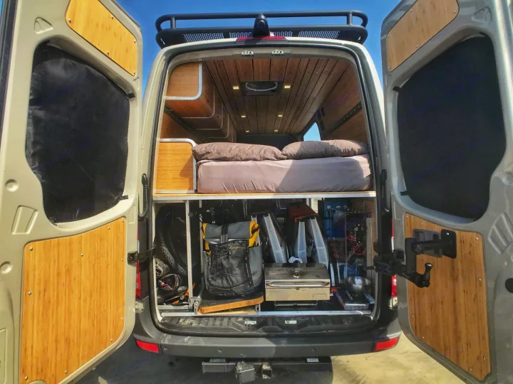 This RV rental showcases a custom camper van's rear: a cozy bed above a spacious gear garage, all with bamboo finishes.. Mercedes-Benz Sprinter 2018