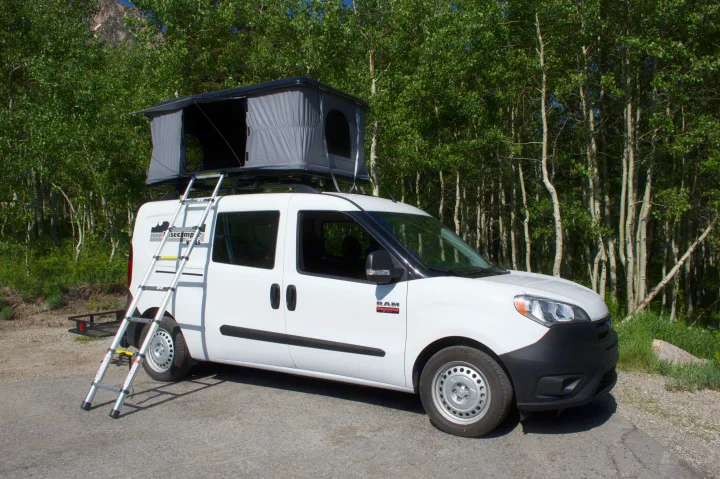 White camper van with a deployed rooftop tent and ladder, ideal for RV rental camping trips and outdoor adventures.. Ram Promaster City 2018