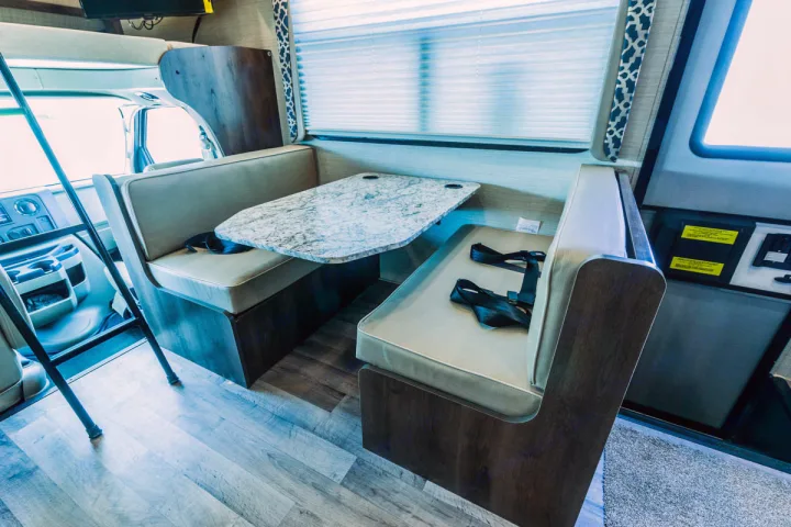 This bright RV rental interior features a stone-look table and two benches with seatbelts, creating a functional dinette space.. Jayco Redhawk 31 XL 2019