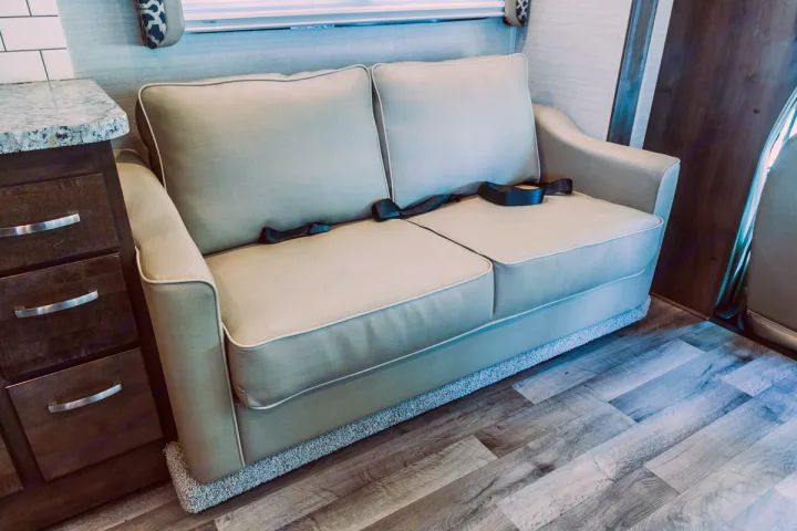 RV rental: A cozy, light-colored sofa with seatbelts and an adjacent storage cabinet, on wood-look flooring.. Jayco Redhawk 31 XL 2019