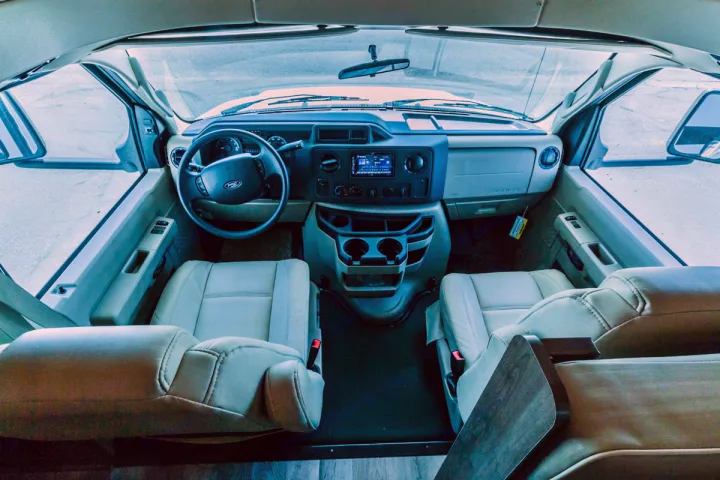 Spacious RV rental cockpit with beige driver & passenger seats, dashboard, and forward view. Ideal for road trips.. Jayco Redhawk 31 XL 2019