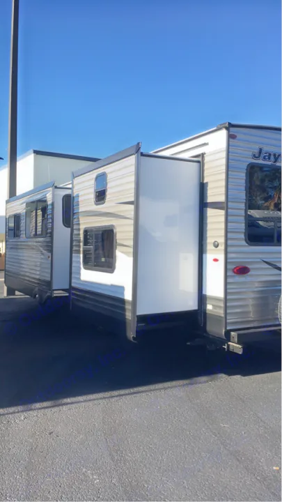 This travel trailer RV rental, with multiple slide-outs extended, is parked on asphalt under a clear blue sky.. Jayco Flight 2018