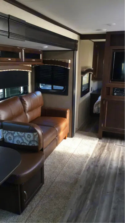 This inviting RV rental offers a comfortable brown sofa, dining booth, and modern dark wood interior, creating a cozy mobile living space.. Jayco Flight 2018