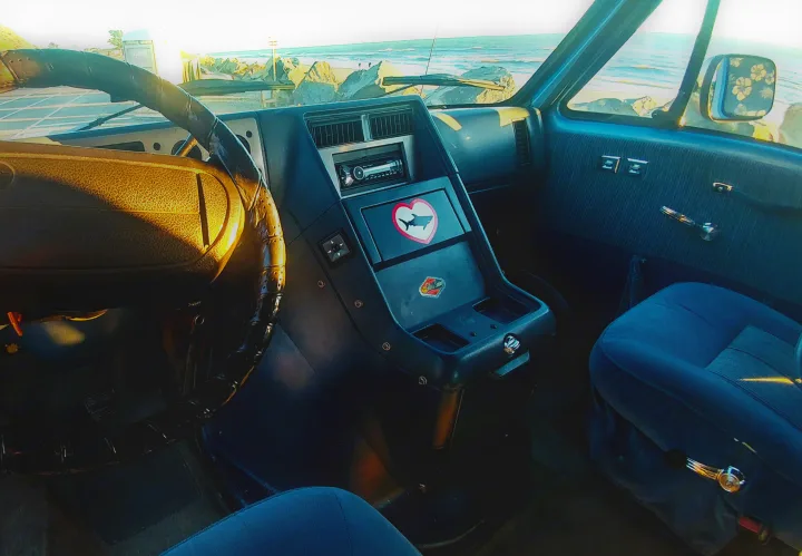 Cozy RV rental interior with ocean view. Dashboard, steering wheel, and blue seats visible, plus a fun shark heart sticker.. Chevrolet Other 1989