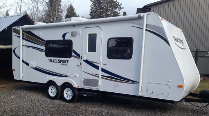 Exterior view of a white Trail Sport RV rental with an extended awning, parked on gravel.. R-Vision TS 24BH 2011
