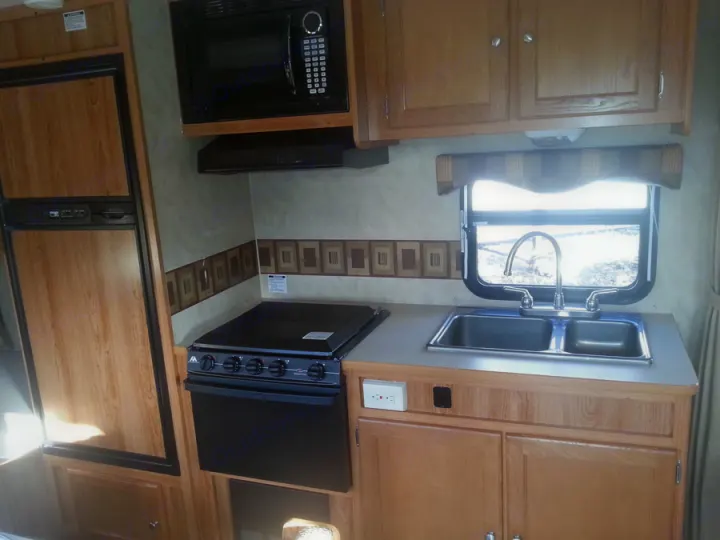 Compact kitchen in an RV rental, featuring a refrigerator, microwave, stove/oven, and double sink for travel convenience.. R-Vision TS 24BH 2011