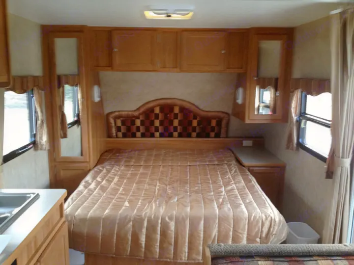 Cozy RV rental bedroom featuring a checkered headboard, comfortable bed, overhead cabinets, and bright windows.. R-Vision TS 24BH 2011