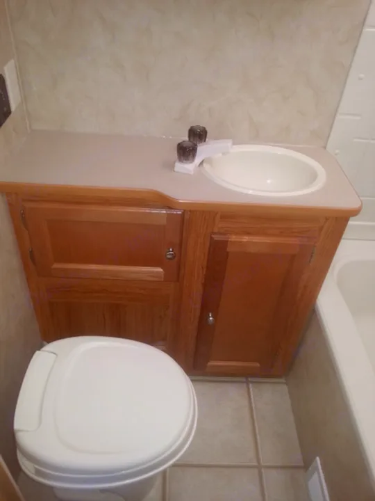 RV rental bathroom: compact vanity with sink & toilet. Wood cabinets, tiled floor, white fixtures, light walls.. R-Vision TS 24BH 2011