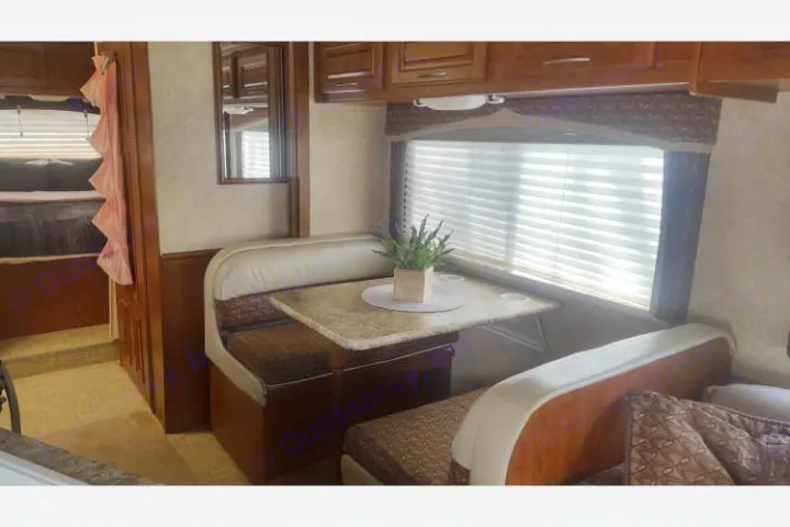 RV rental interior: A cozy dinette with a plant, wood cabinets, a window with blinds, and a glimpse of the bunk beds.. Ford E450 Fourwinds Chateau 2010