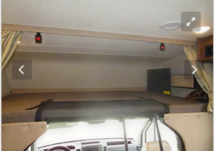 Cozy RV rental cab-over bunk with bed, TV, and safety net, looking forward over the dashboard.. Mercedes-Benz 313 Sprinter LWB Motorhome 2018