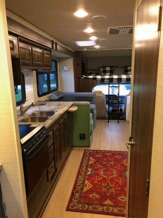 Bright RV rental interior featuring a kitchen, green dinette, bunk bed, and a colorful rug on the floor.. Jayco Greyhawk 2018
