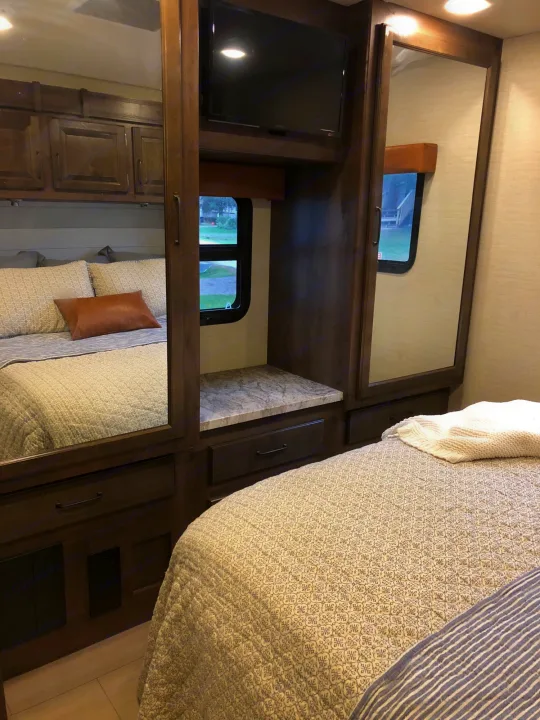 Cozy RV rental bedroom featuring a neatly made patterned bed, dark wood cabinets, TV, and mirrored wardrobe for storage.. Jayco Greyhawk 2018