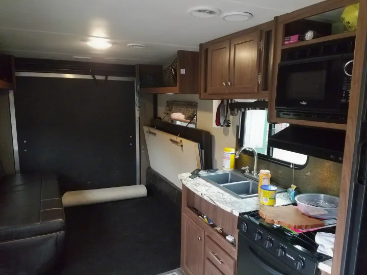 RV rental interior featuring a functional kitchen with sink, stove, microwave, and a versatile rear area with a bench and folded bed.. Heartland Pioneer 2016