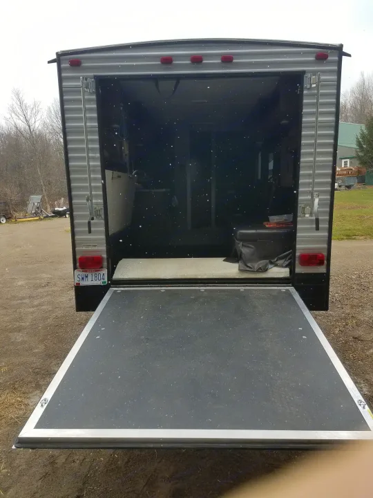 Rear of an RV rental trailer with a lowered ramp. Interior shows equipment space. Ohio plate SWM 1804, snowing lightly.. Heartland Pioneer 2016