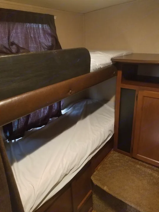 Cozy bunk beds with white sheets provide comfortable sleeping space in this RV rental. Dark curtains and wood accents complete the interior.. Jayco White Hawk Ultra Lite 2015
