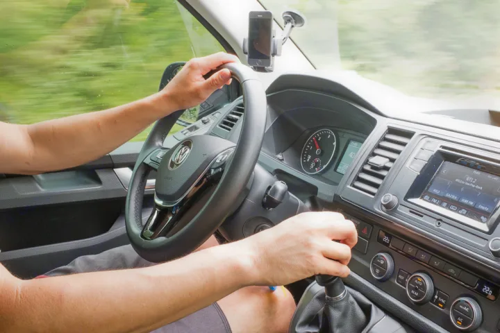 Driver's view of an RV rental interior while on a road trip, showing hands on the steering wheel, gear shift, and dashboard.. Volkswagen Caravelle Long 2019