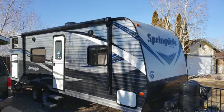 An RV rental: a modern Springdale travel trailer with an awning, parked outdoors under a clear sky.. Keystone RV Springdale 2018