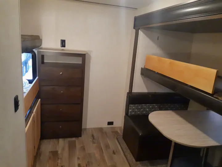 Inside an RV rental: view of bunk beds, a dinette, and a brown dresser against light walls.. Starcraft Autumn Ridge 2018
