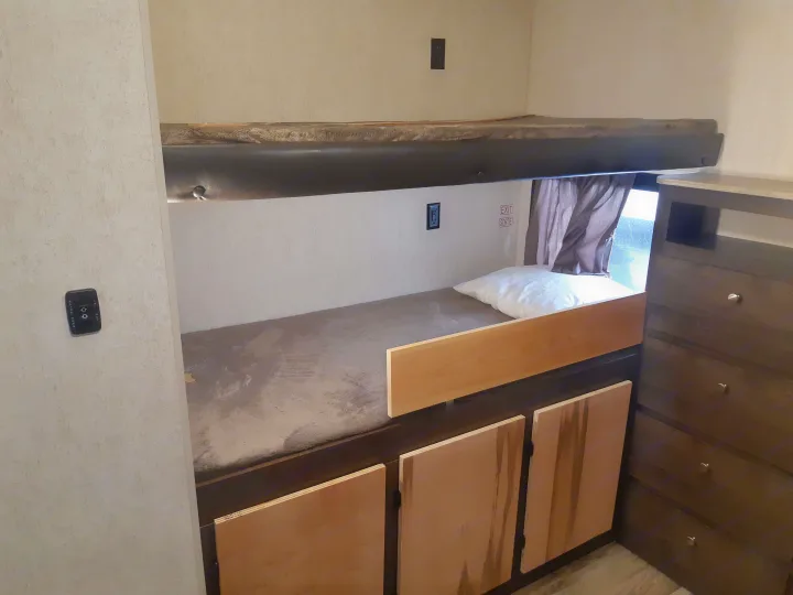 RV rental bunk bedroom featuring upper and lower bunks with mattresses, built-in storage, and a dresser on the right.. Starcraft Autumn Ridge 2018